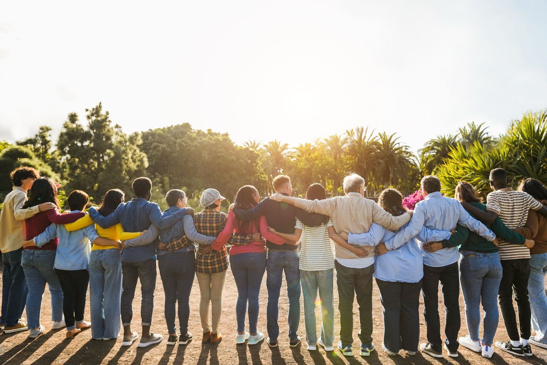 A line of people standing with their arms around each other's shoulders at sunset.