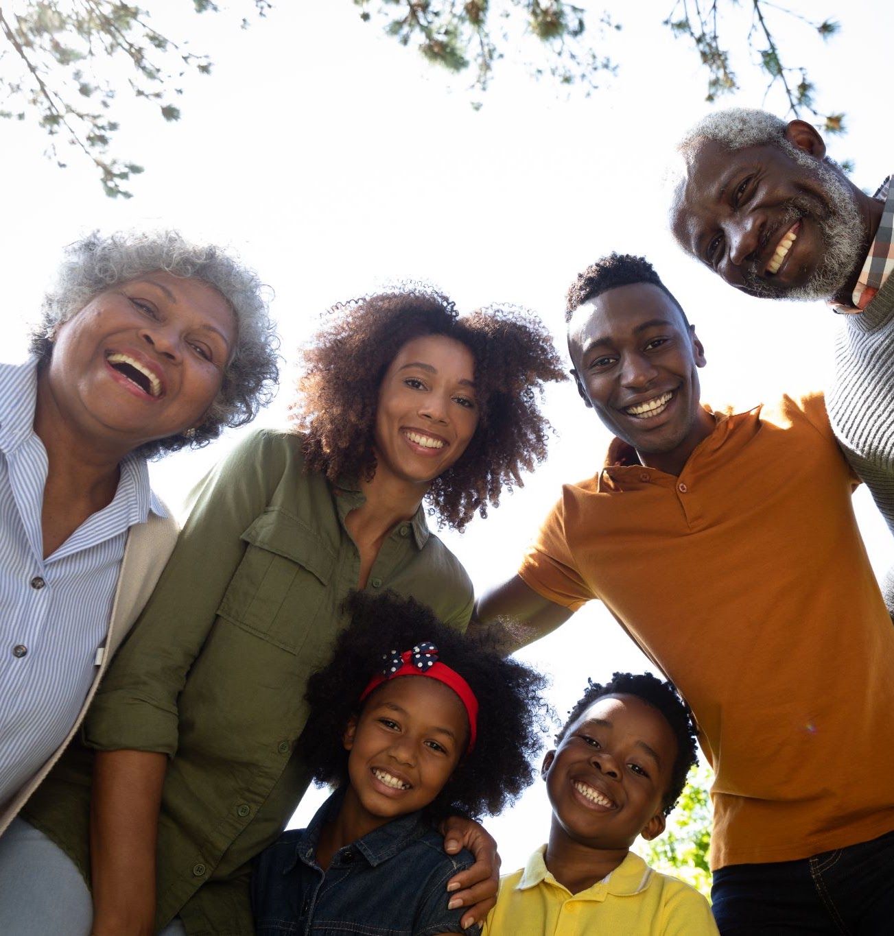 A group of people of different ages standing together and smiling upward.