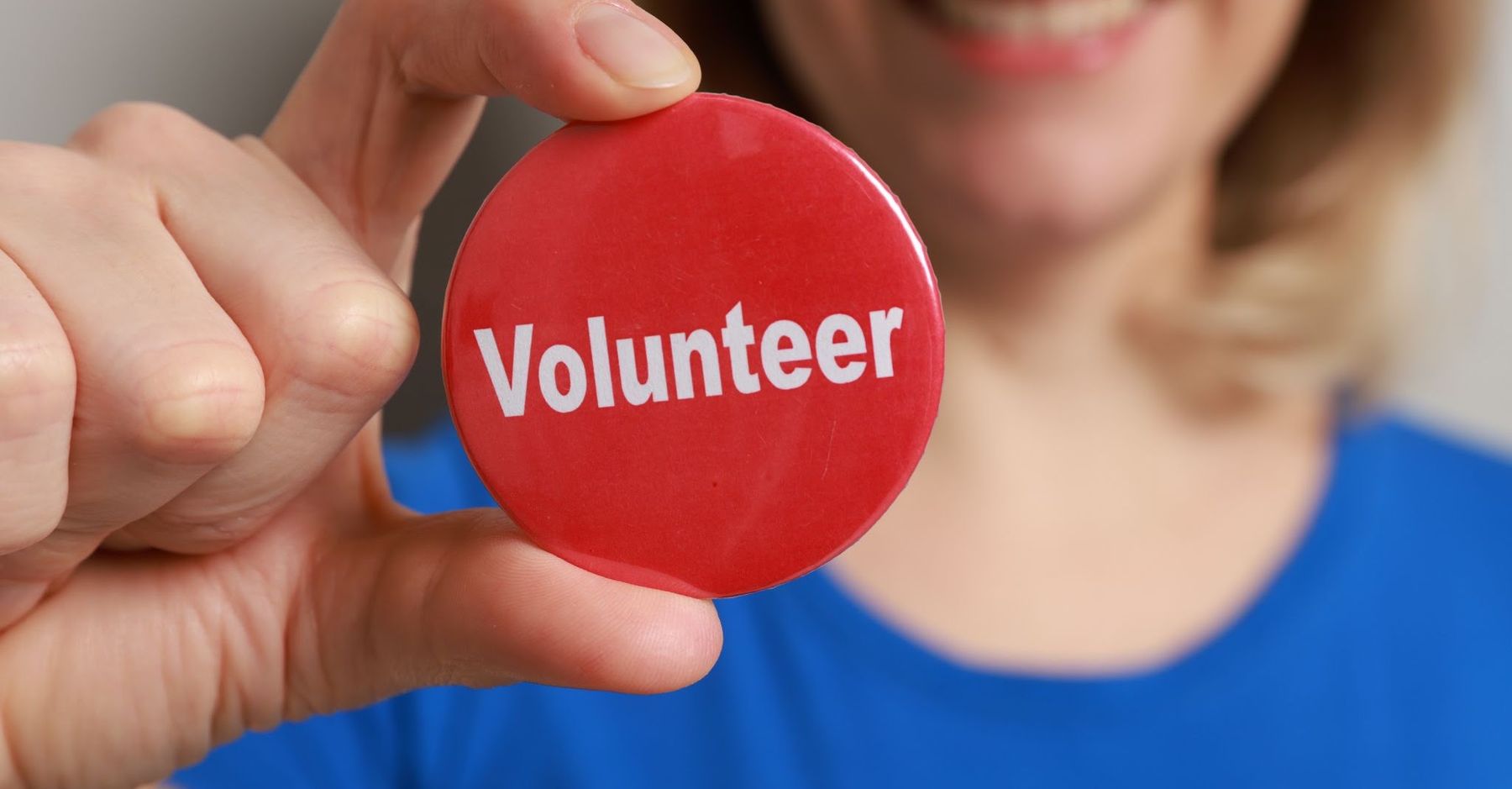 A person holding up a round red badge that reads Volunteer.